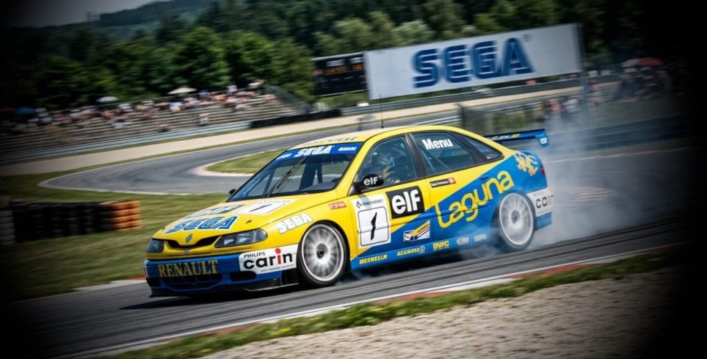 Renault Laguna Super Touring con diseño SEGA circulando a alta velocidad en el circuito de Brno con interfaz de RaceRoom.